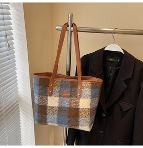 Detail of wool plaid tote bag texture with brown leather handles and gold rivets