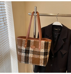 Detail of checkered wool tote bag with leather strap hanging against a neutral background