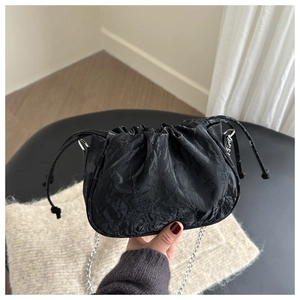 Detail of black pleated bucket bag with silver chain strap and drawstring closure