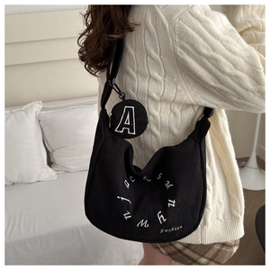 Detail of black corduroy hobo bag with white letter embroidery and a small round pouch