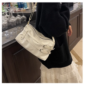 Close-up of white glossy pleated shoulder bag with double buckles and silver hardware details