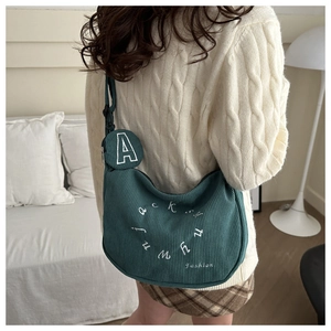 Close-up of green corduroy crescent shoulder bag with letter embroidery and round coin purse