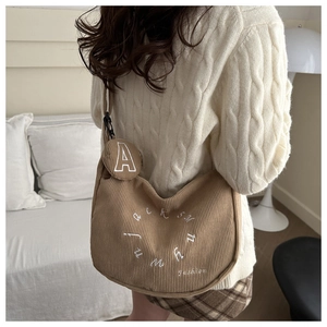 Détail d'un sac demi-lune en velours côtelé marron avec broderie porté à l'épaule