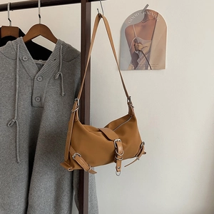 Brown faux leather shoulder bag with silver buckles in trendy biker style on a hanger