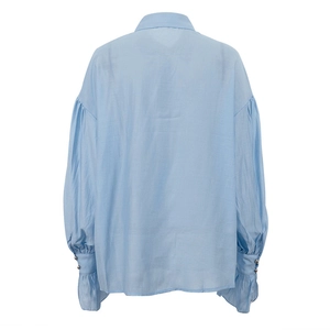 Dettaglio di una camicia celeste con polsini a volant e bottoni decorativi in metallo