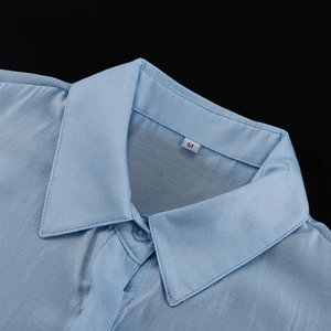 Dettaglio del colletto di camicia azzurra con etichetta taglia M su tessuto pregiato