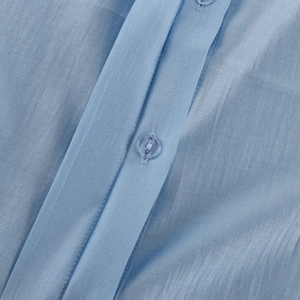 Dettaglio dell'abbottonatura camicia azzurra con trama e bottone coordinato