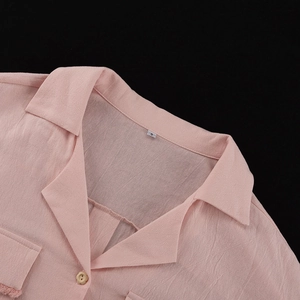 Detail of pink cotton shirt featuring a yellow flower button and textured lapel collar