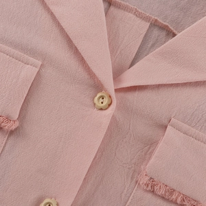 Macro detail of pink textured cotton shirt featuring lapel collar and floral button