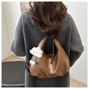 Dettaglio di una borsa tote in pelle marrone con ciondolo a nuvola su cappotto grigio