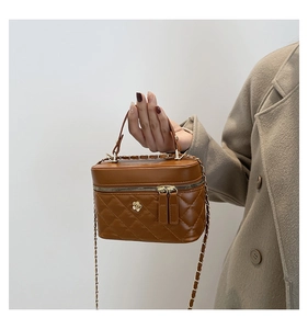 Detail of a brown quilted leather box bag featuring a gold flower clasp and chain strap