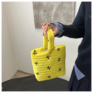 Detail of yellow quilted tote bag featuring black bow embroidery and horizontal stitching
