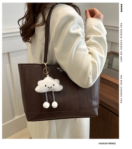 Close-up of a brown quilted tote bag with a cute white cloud plush charm on a model