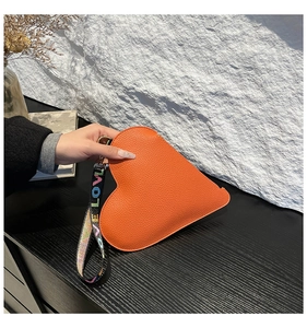 Détail du sac à main orange en forme de cœur avec bandoulière Love sur mur texturé