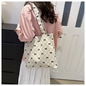 Détail d'un sac cabas en toile crème avec motif de nœud noir et bandoulière large imprimée