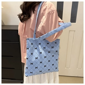 Detail of light blue corduroy tote bag with bow print worn over the shoulder by a model