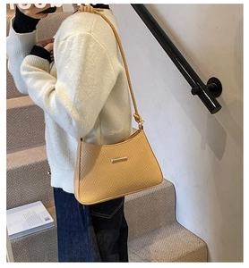 Detail of beige shoulder bag featuring geometric texture and gold metal bar accent