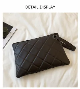 Detail of dark brown quilted clutch bag with rhombus pattern and wrist strap on white fabric
