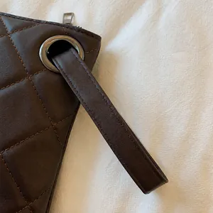 Detailed macro view of dark brown quilted leather bag with metallic eyelet and strap