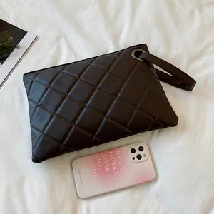 Macro detail of brown quilted pattern on minimalist leather clutch bag with smartphone size reference
