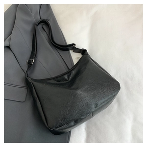 Detail of black crossbody bag featuring pleated faux leather texture and silver metal buckle