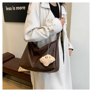 Detail of dark brown PU leather tote with a plush smiley face pendant and wide strap