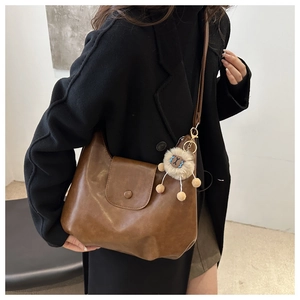 Brown leather shoulder bag with a curved flap and a cute lion plush keychain accessory