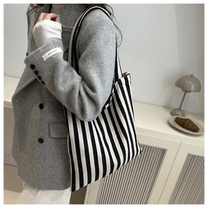 Detail of a large black and white striped canvas tote bag worn with a grey blazer