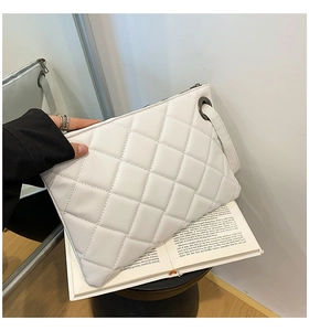 Detail of white quilted crossbody bag with metal zipper and wrist strap on book