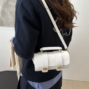 White cylinder crossbody bag with floral embossing and gold buckles on a navy sweater