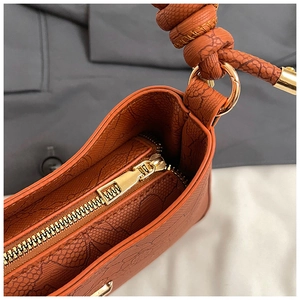 Detail of caramel snakeskin texture shoulder bag with gold zipper and knotted strap