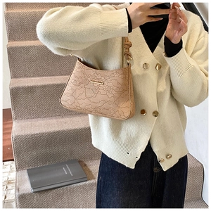 Detail of embossed floral pattern and knot strap on beige faux leather baguette bag