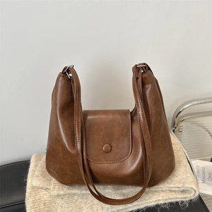 Retro brown PU leather tote bag with round buckle on cozy beige knit blanket
