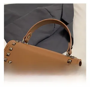 Close-up of brown crossbody bag with metal rivets, top handle, and silver buckle detail