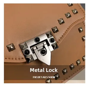 Macro shot of silver pyramid studs and push-lock buckle on textured tan leather handbag