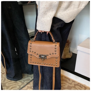 Detail of brown matte leather bag featuring silver square rivets and metal lock closure