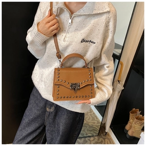 Detail view of brown square shoulder bag with punk-style metal rivets and top handle