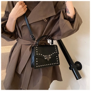 Detail of black crossbody bag with silver square rivets and metal buckle on trench coat