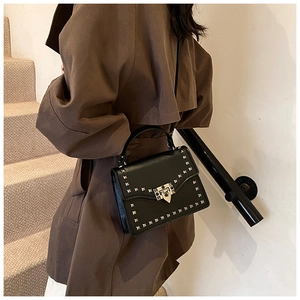 Detail view of black leather crossbody bag with golden studs on a model in a minimal setting