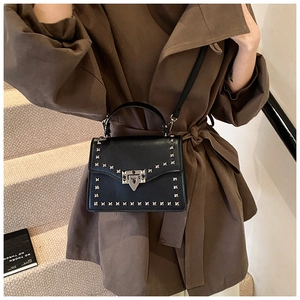 Detail of black leather crossbody bag featuring silver pyramid studs and twist lock