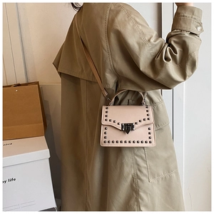 Detail of beige rivet crossbody bag with square metal studs and elegant lock closure