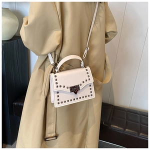 Detail of cream crossbody bag featuring metallic square rivets and vintage metal clasp