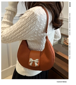 Detail of orange crescent moon shoulder bag with vertical stripe texture and bow charm