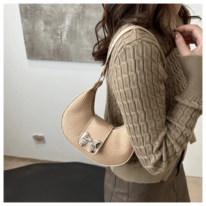 Détail du sac croissant beige avec texture plissée et décoration de nœud en métal argenté