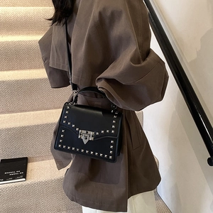Black leather crossbody bag with silver studs and chain strap on a stylish woman