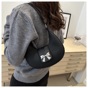 Détail d'un sac à bandoulière noir en demi-lune avec nœud argenté et texture plissée