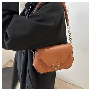 Close-up of a brown leather shoulder bag with gold chain strap worn over a black coat
