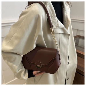 Detail of dark brown leather handbag featuring a round gold buckle and chain strap