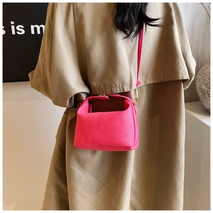 Detail einer pinkfarbenen Webstruktur-Handtasche mit goldenem Verschluss auf Trenchcoat