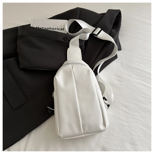 Close-up of a white PU leather chest bag with a wide strap on a black blazer jacket